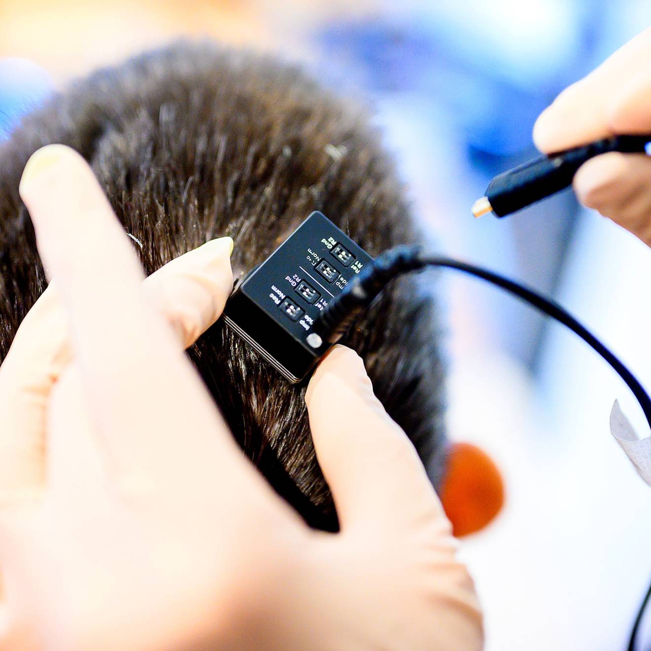 A close-up view of a pair of hands holding a small device about to be plugged in over someone's head