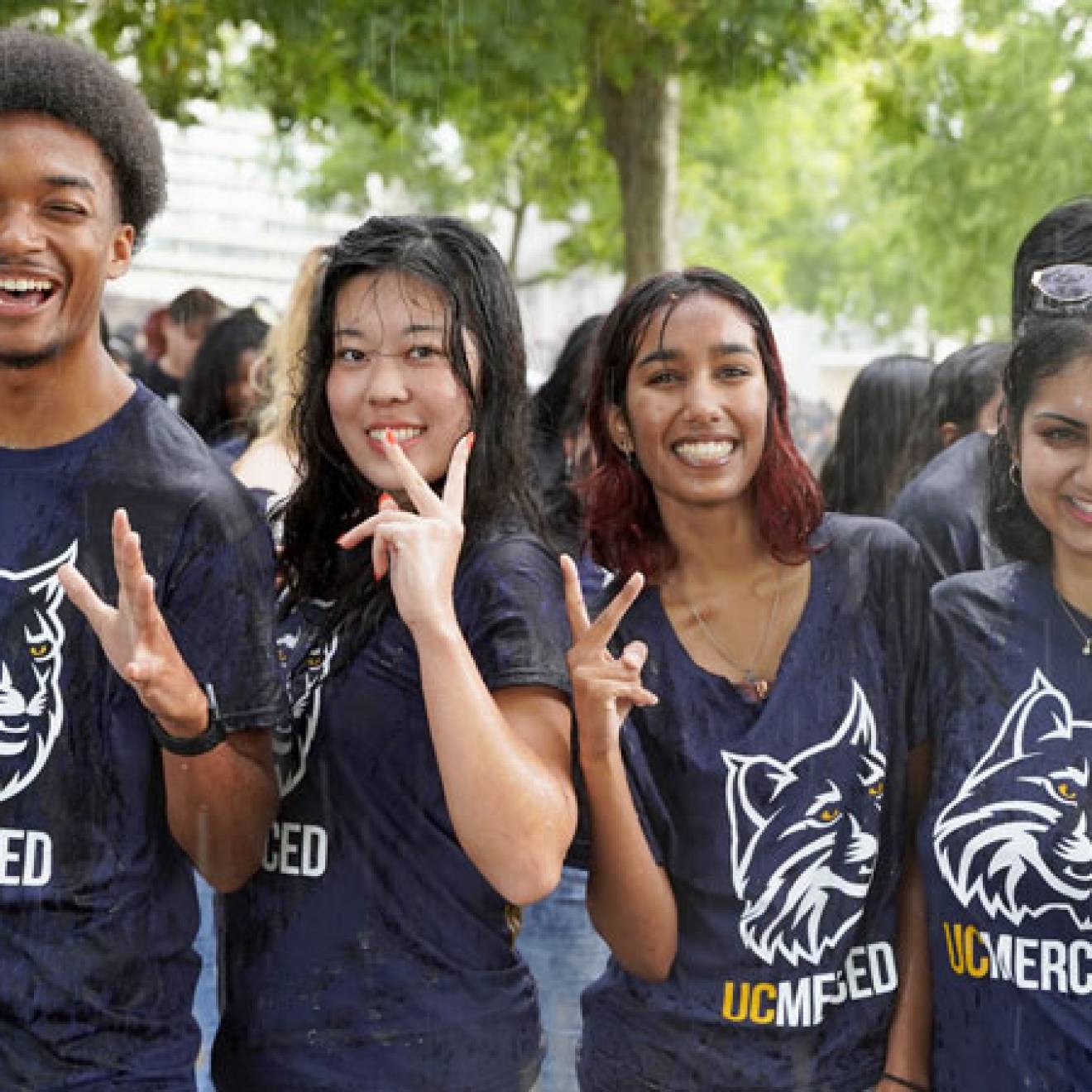 Five students wearing UC Merced Bobcat t-shirts smile for the camera in a downpour