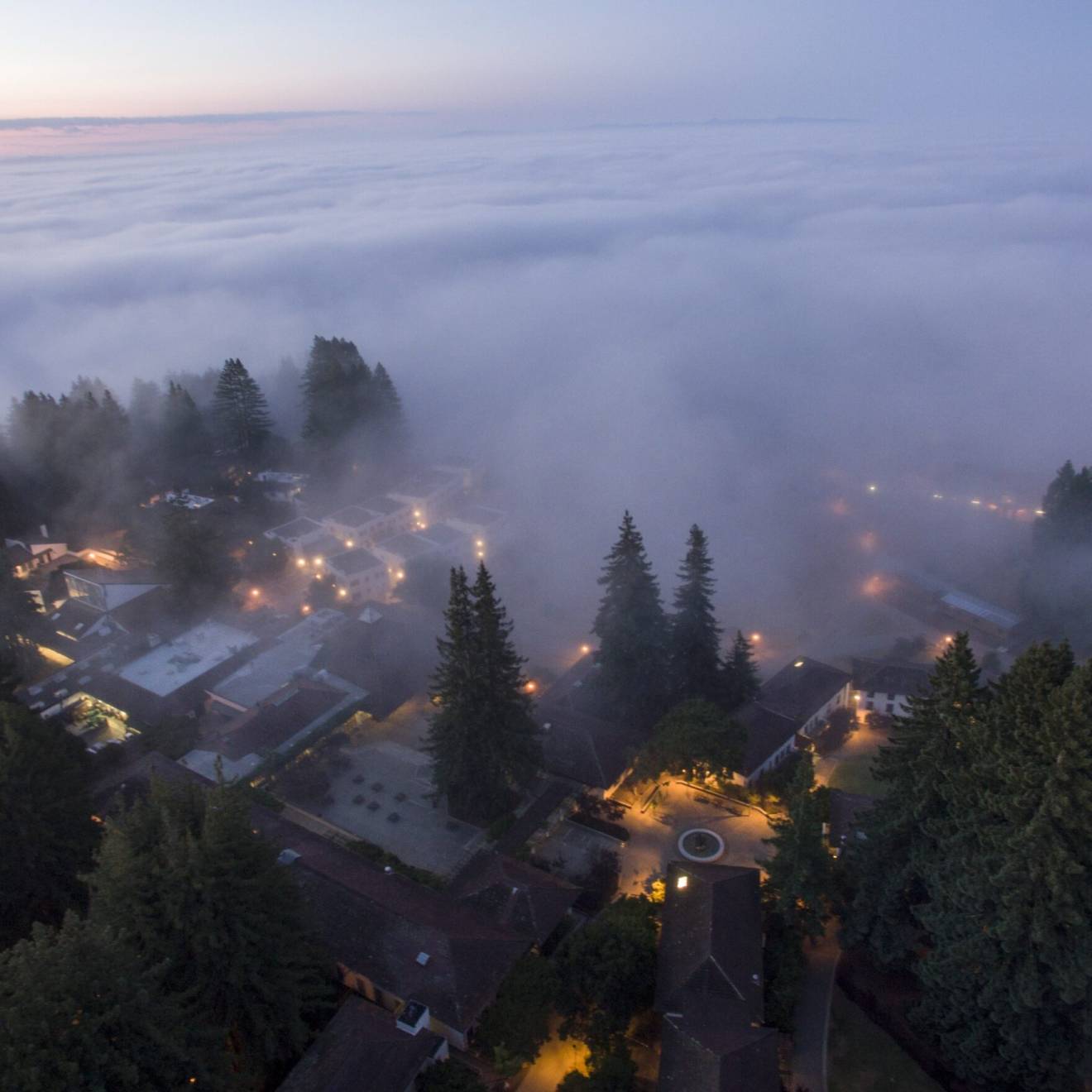 A view from above of heavy fog rolling from a reddish sky over a twilit UC Santa Cruz campus