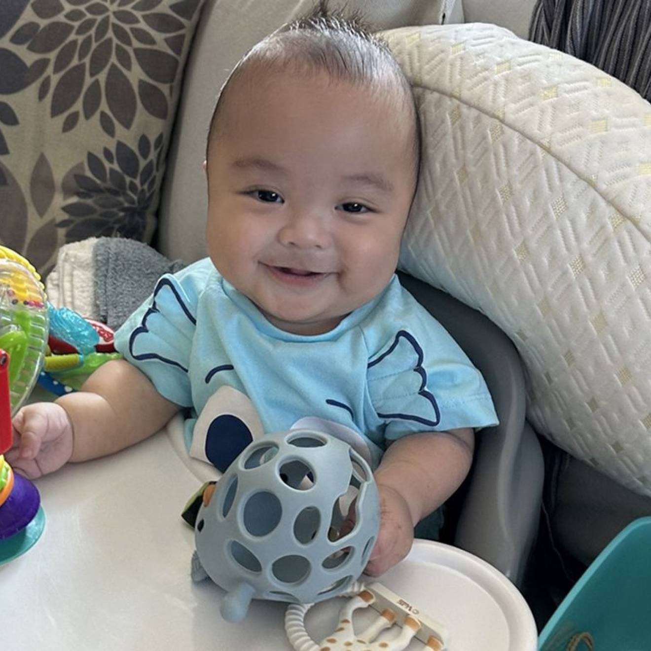 A baby smiles at the camera and plays with toys in a bouncy seat