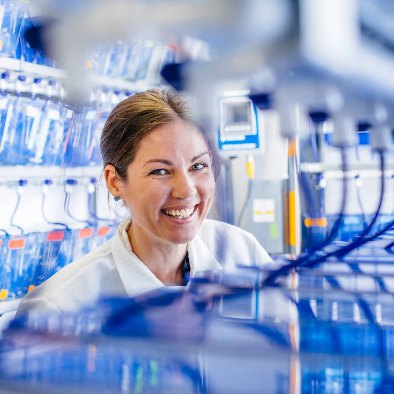 A student researcher smiles in a lab coat around blue tubing