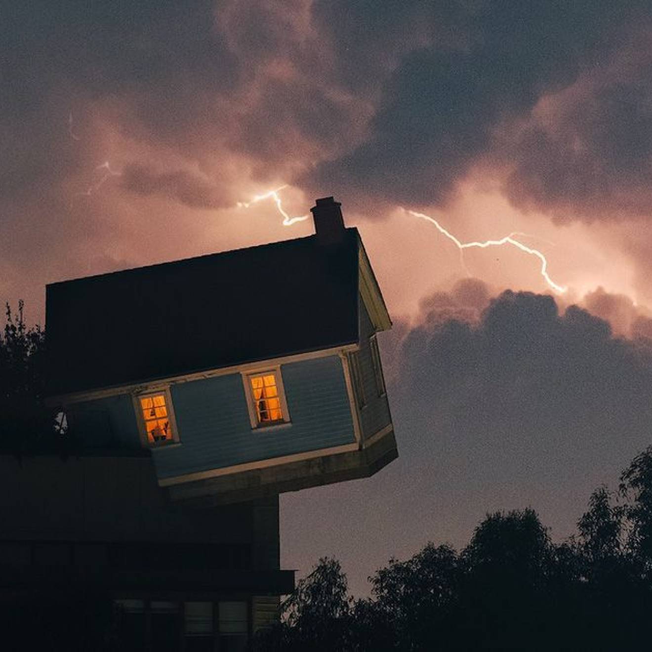 The leaning/falling house installation on the UC San Diego campus with a lightning sky backdrop
