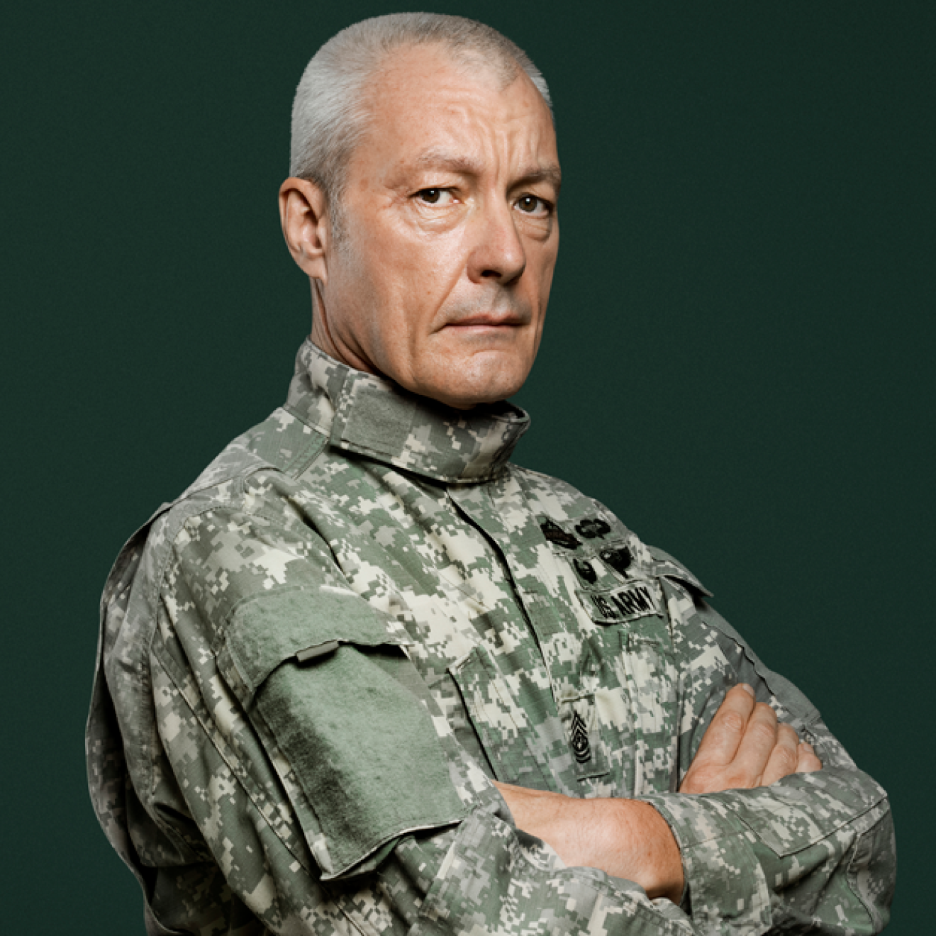 A man in military uniform stands with his arms folded across his chest.