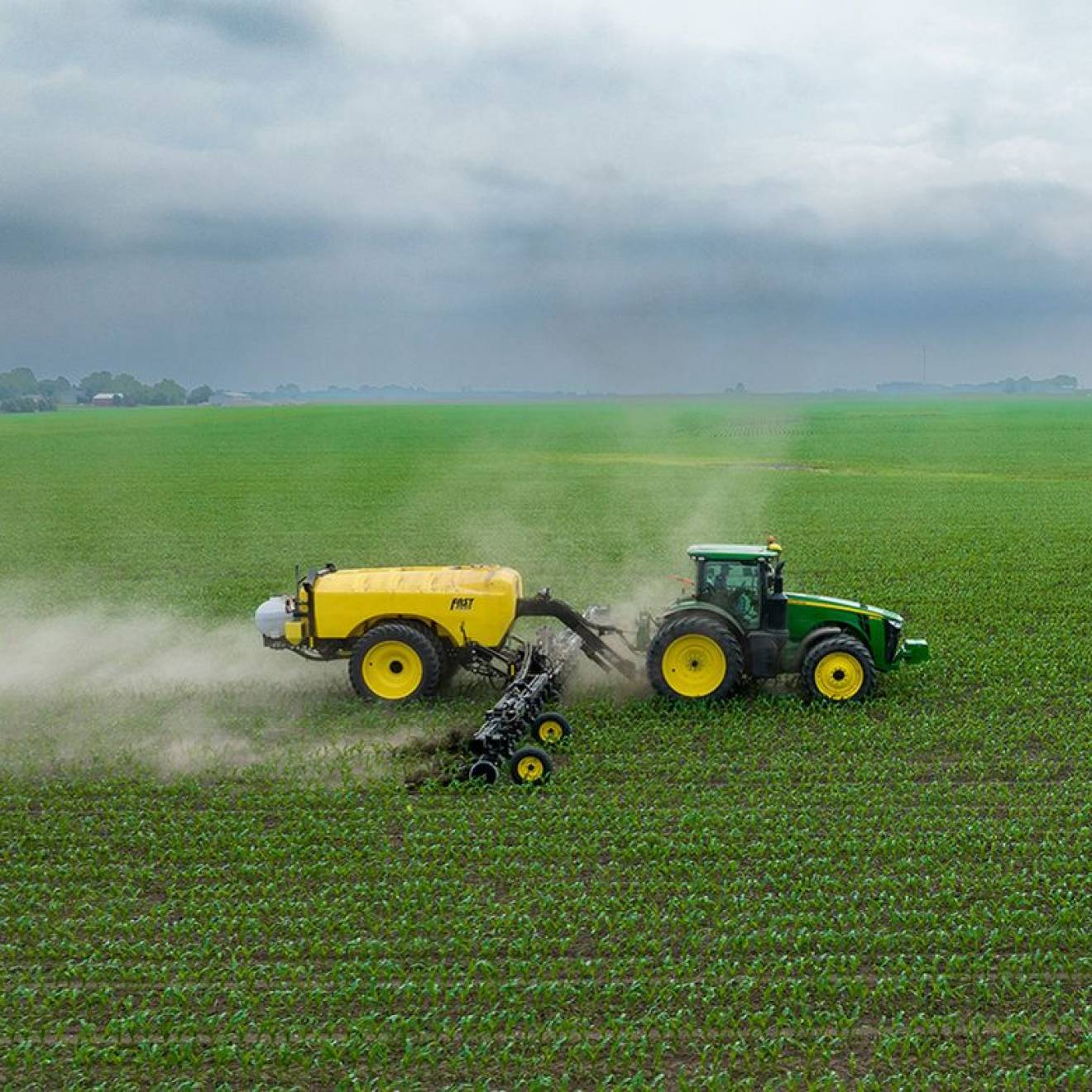 A tractor sprays pesticides on a green field under a gray sky