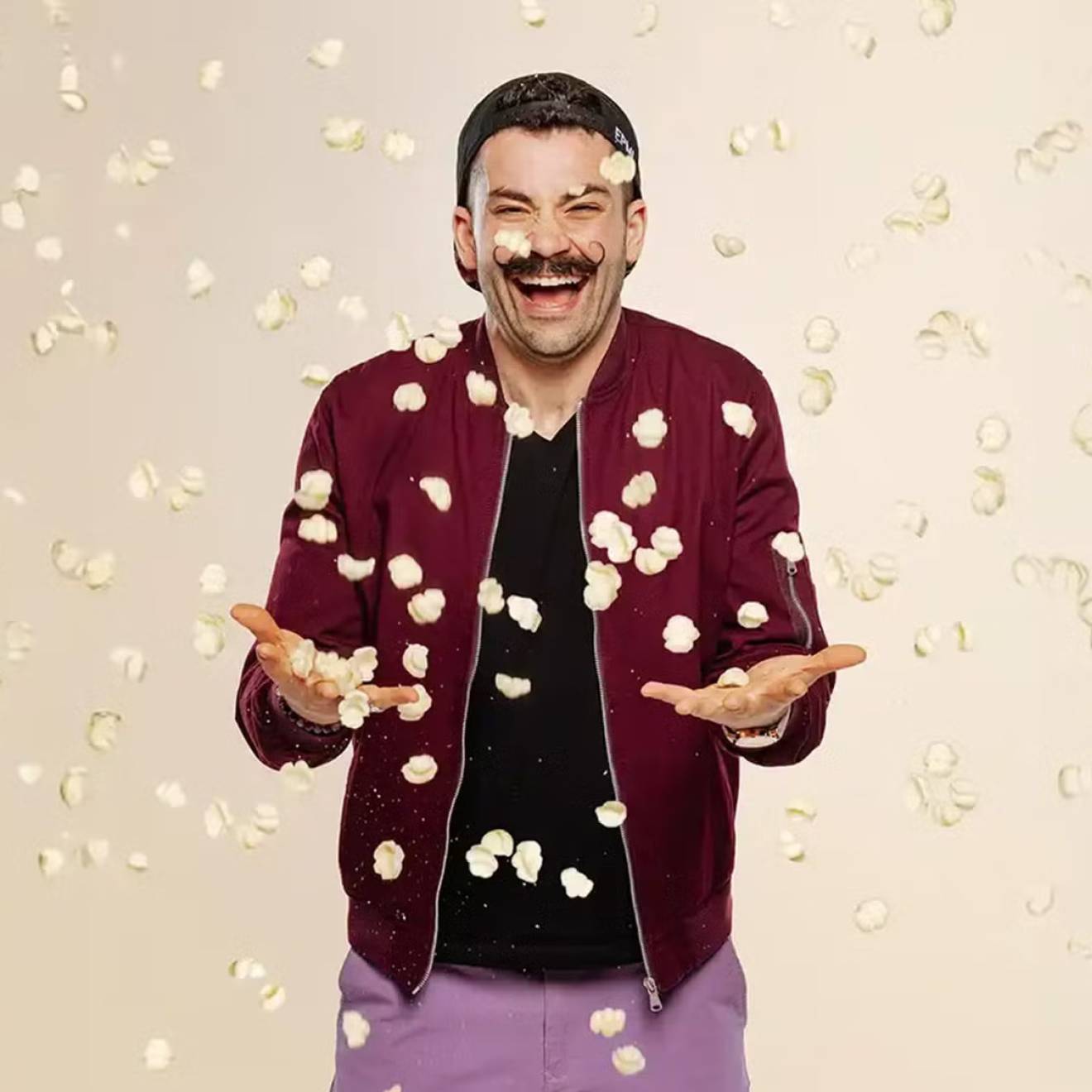 Laughing man in magneta jacket and mustache while pasta chips fall around him