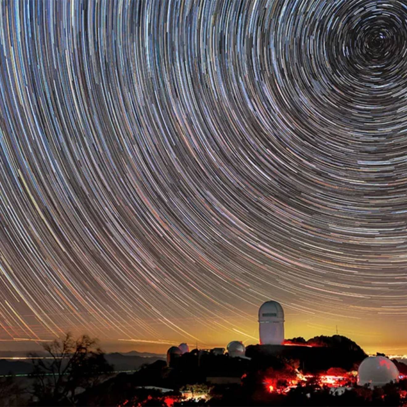 A telescope on a mountain peak at sunset, taken using time lapse to show concentric circles of star trails in the sky