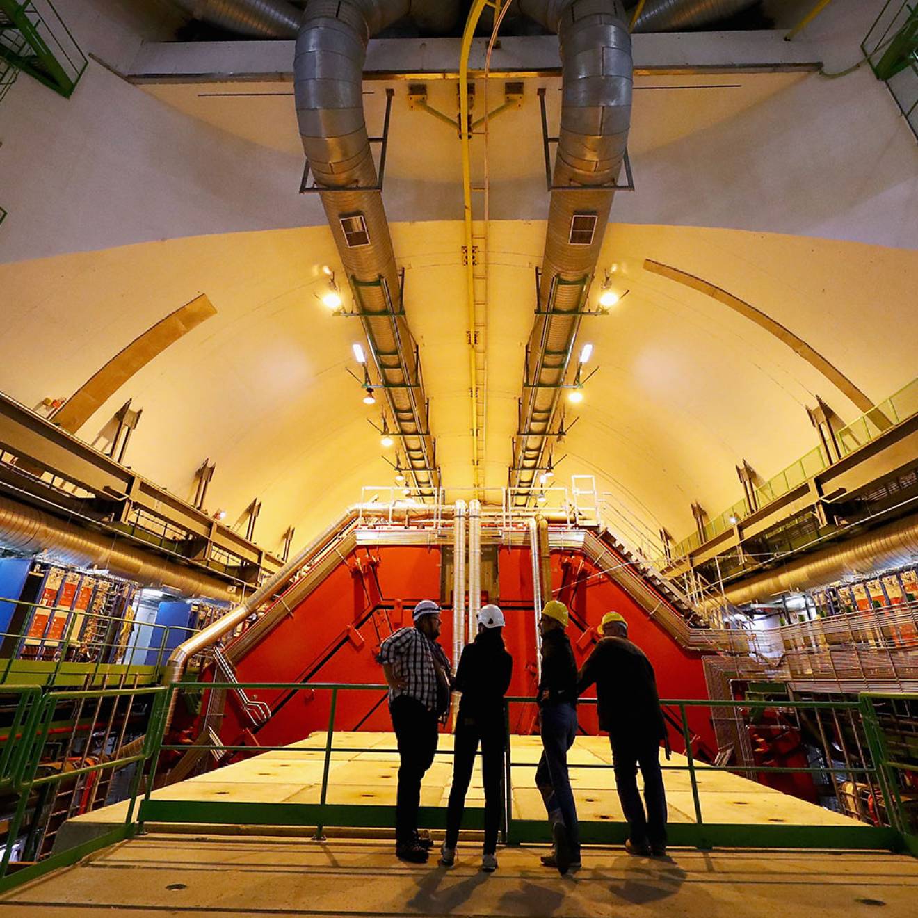 Four people stand backlit in a giant room full of high-tech machinery