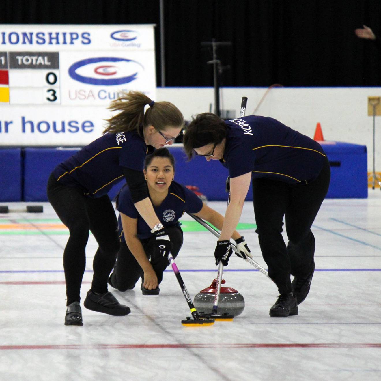 Three women curling, one delivering the stone, two sweeping