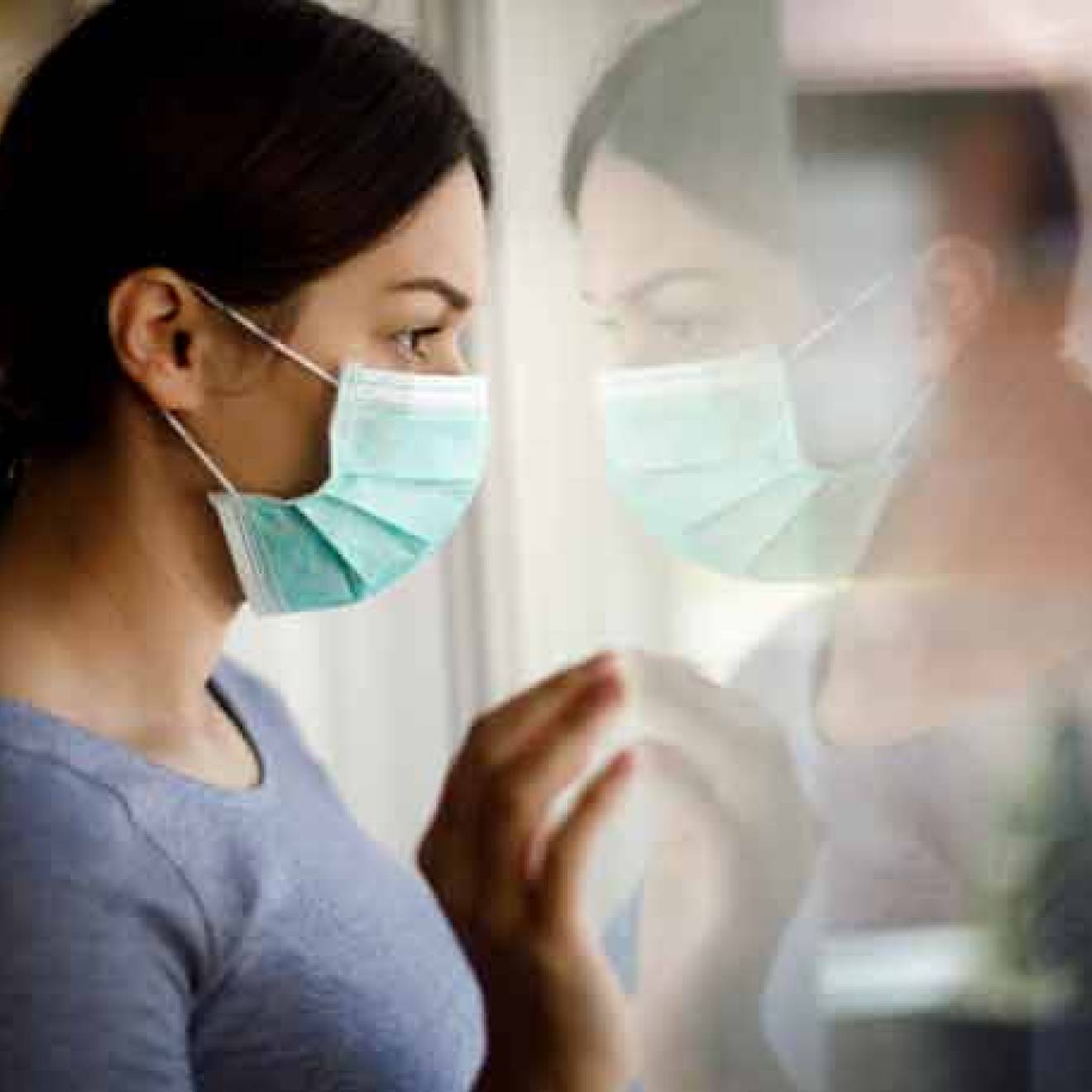 Woman wearing mask looking outside, forlorn