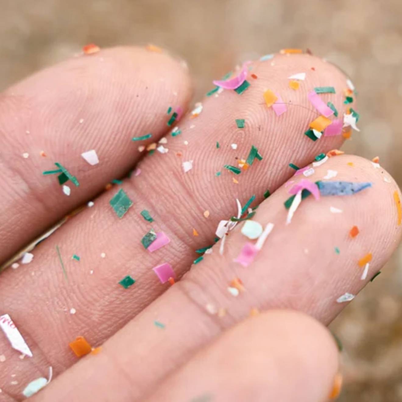 Close-up of a person's upturned palm and fingers with tiny shards of multi colored plastic stuck to the skin.