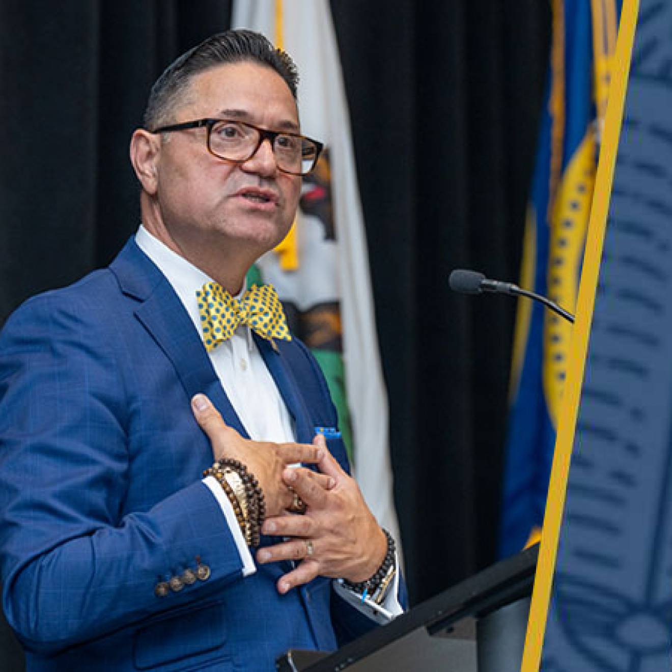 Juan Sánchez Muñoz in a blue suit speaks at a podium, holding both hands to his chest