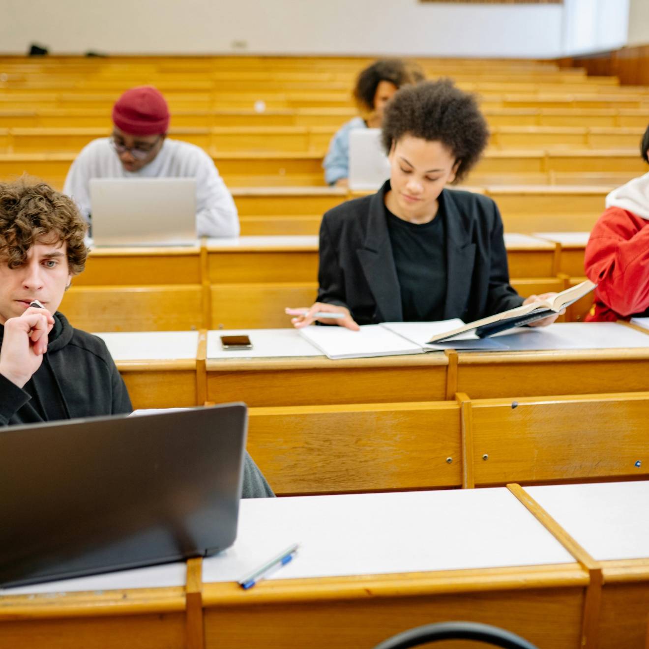 Five students in four rows of a lecture hall work independently