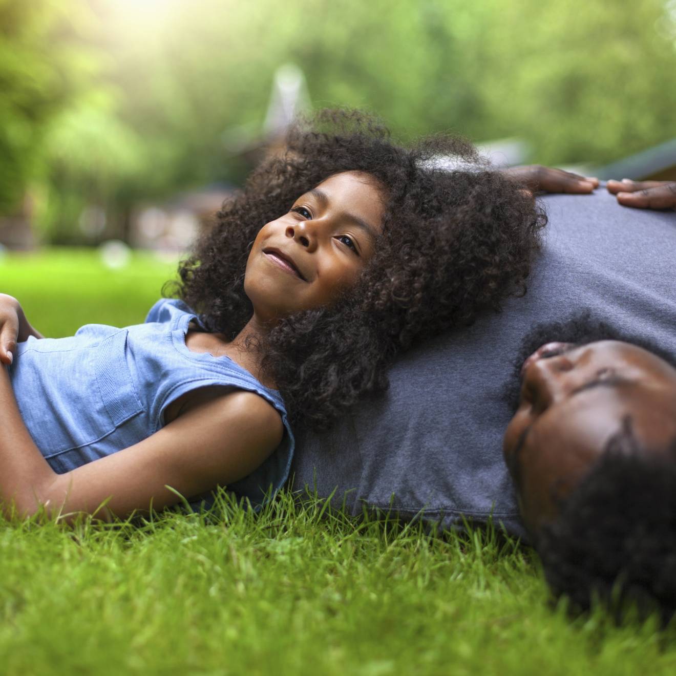 A young girl reclines against her father's shoulder on fresh grass