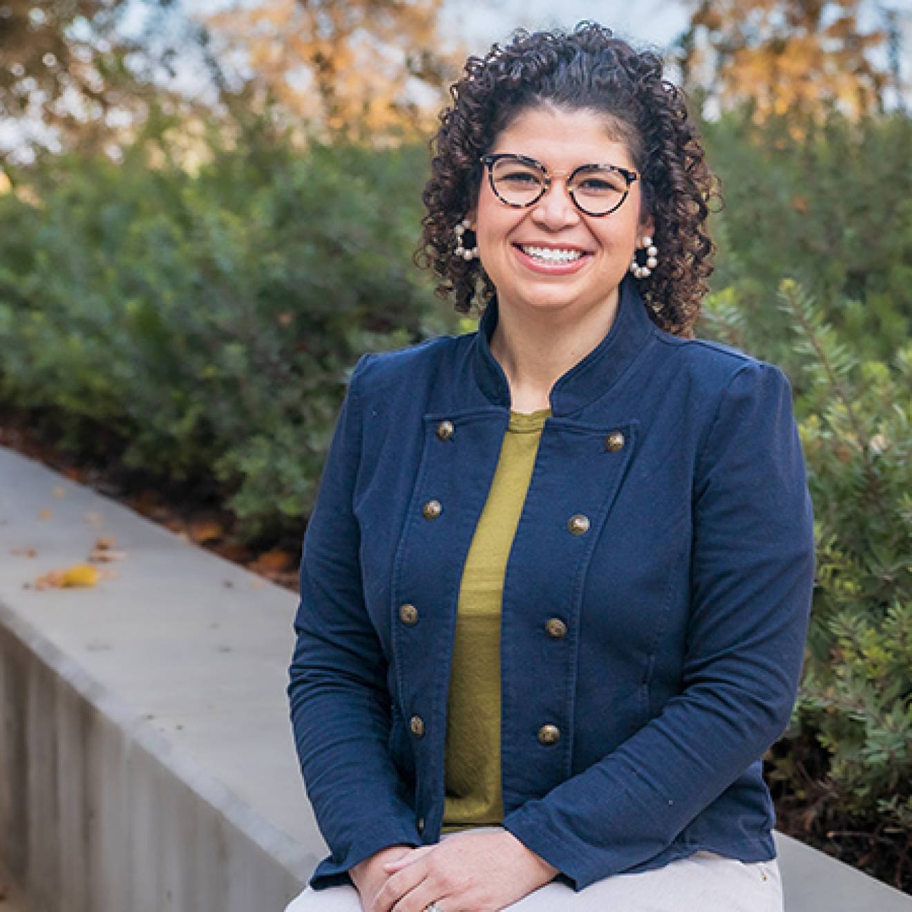 A woman sits on a wall in front of shrubbery