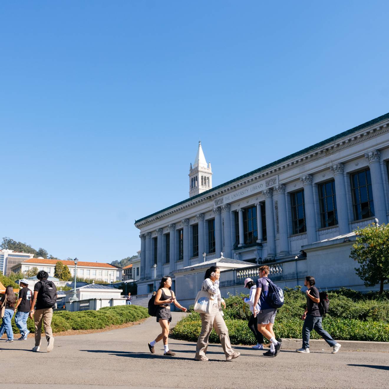 Students walk on the UC Berkeley campus, Campanile behind them
