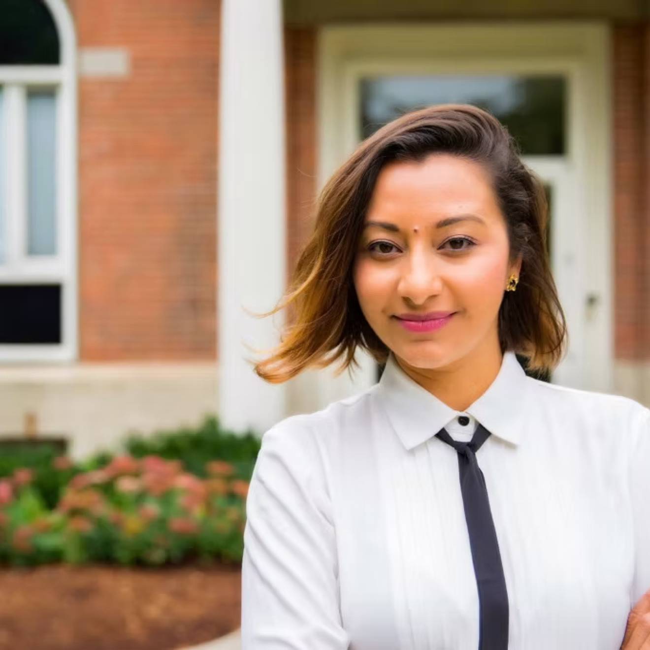 A woman with a skinny tie and arms crossed smiles at camera