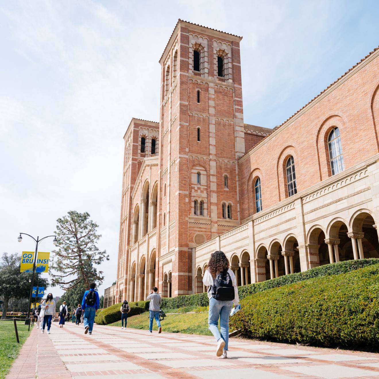 Royce Hall on the UCLA campus, a light adobe brick building, photographed from a low angle and at the side as a few students walk