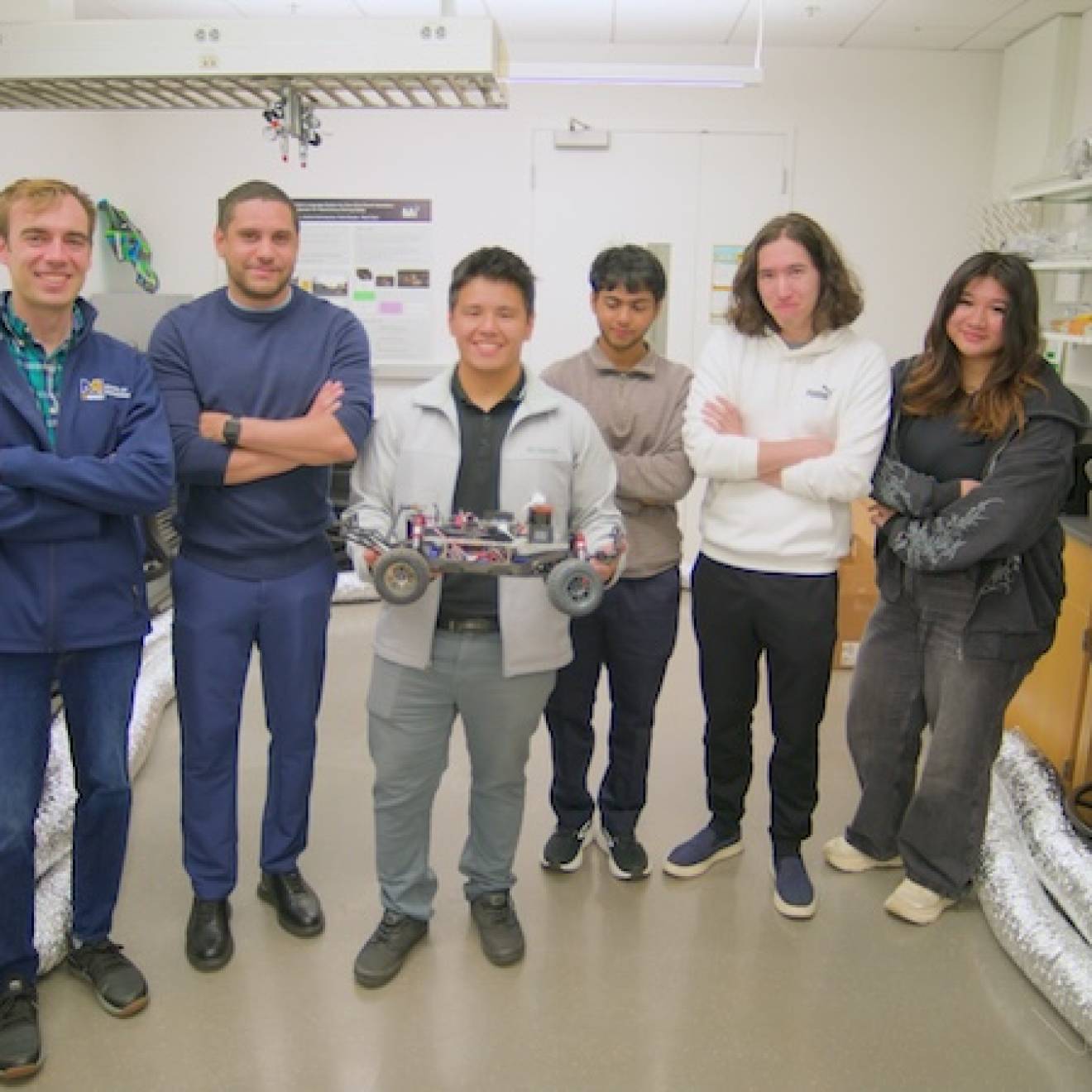 6 people stand in a lab, one holding a small robotic car