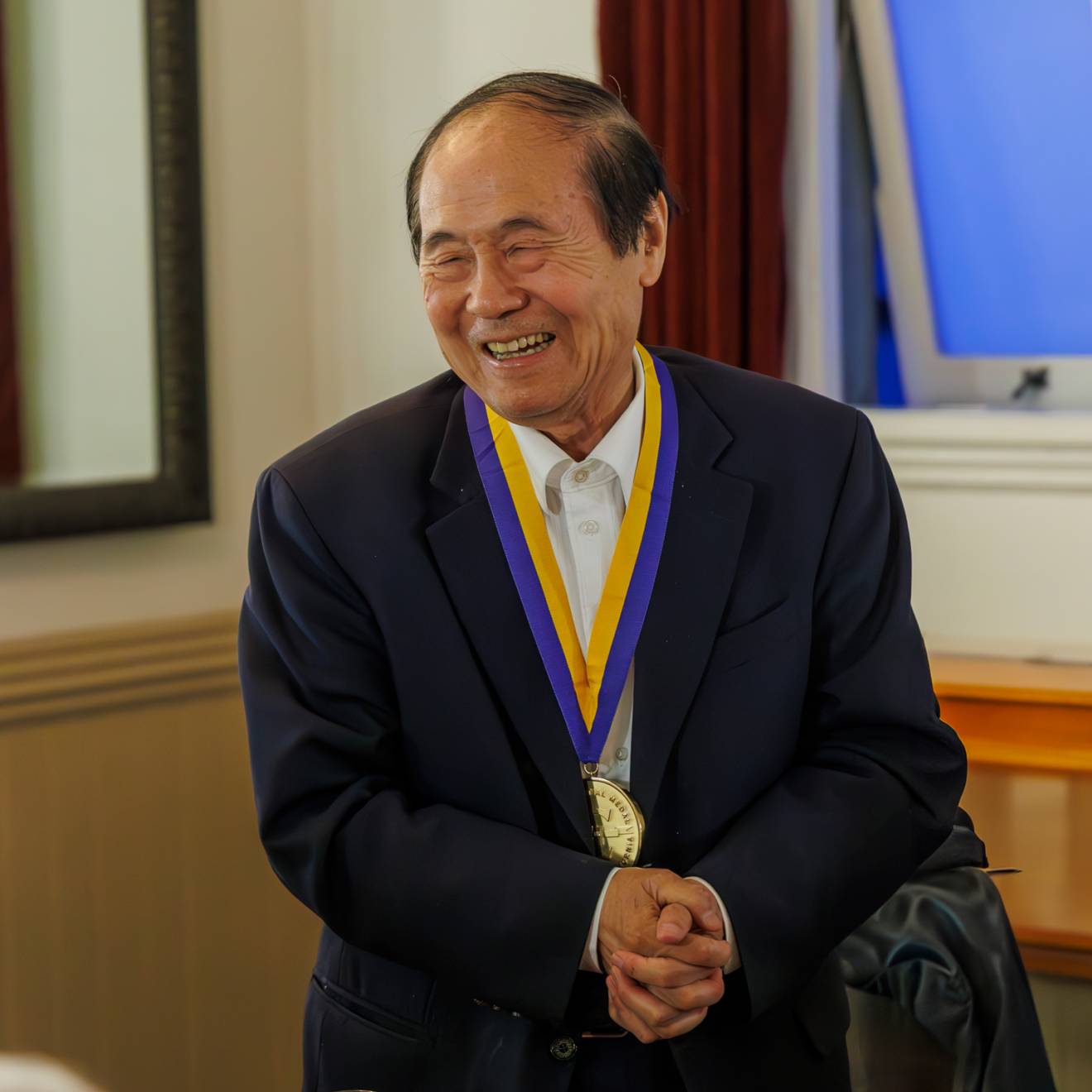 Chancellor Henry T. Yang smiles widely with his hands clasped as he wears his UC Presidential medal